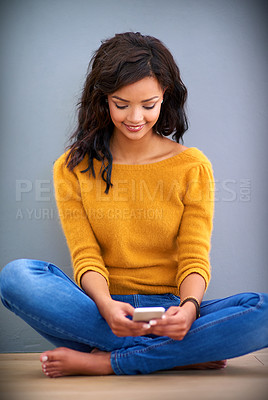 Buy stock photo Shot of a young woman sitting on the floor and using her mobile phone