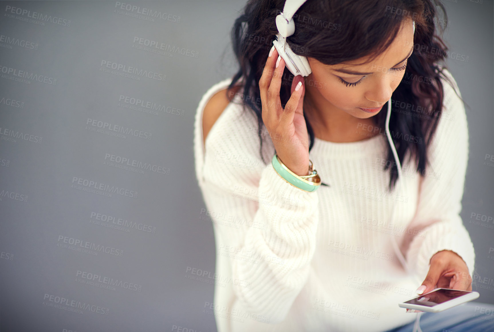 Buy stock photo Studio shot of a young woman listening to music while using her phone against a gray background