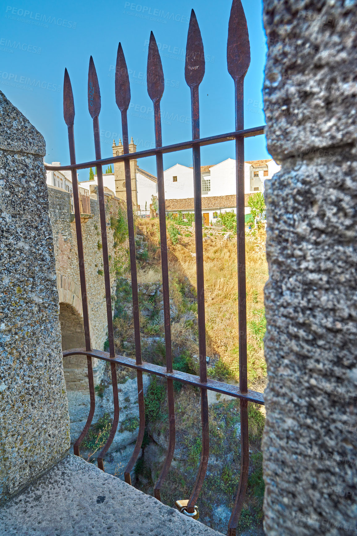 Buy stock photo Iron, fence and bridge in city for architecture, travel or ancient town in Spain. Blue sky, village design or railing in stone for protection, heritage or sightseeing at landmark Ronda for wallpaper