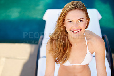 Buy stock photo Shot of a young woman relaxing on a lounge chair beside a swimming pool