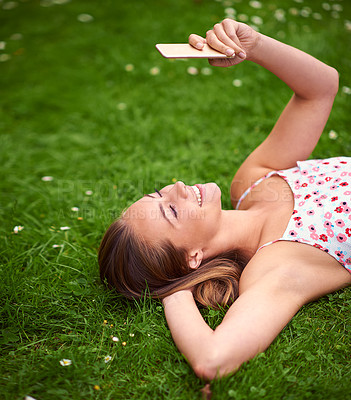Buy stock photo Shot of a young woman using her cellphone while lying on the grass