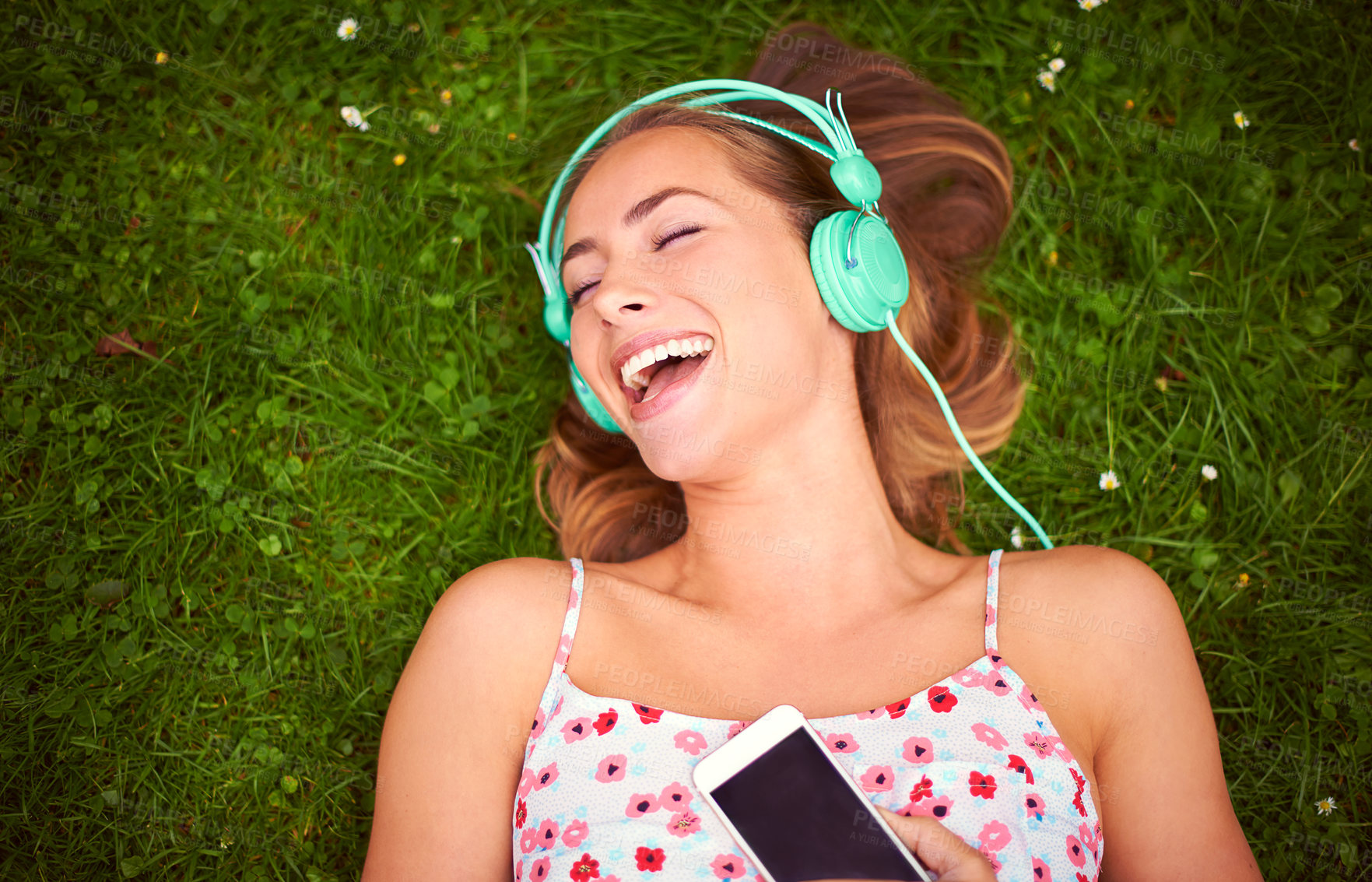 Buy stock photo Shot of a young woman listening to music while lying on the grass