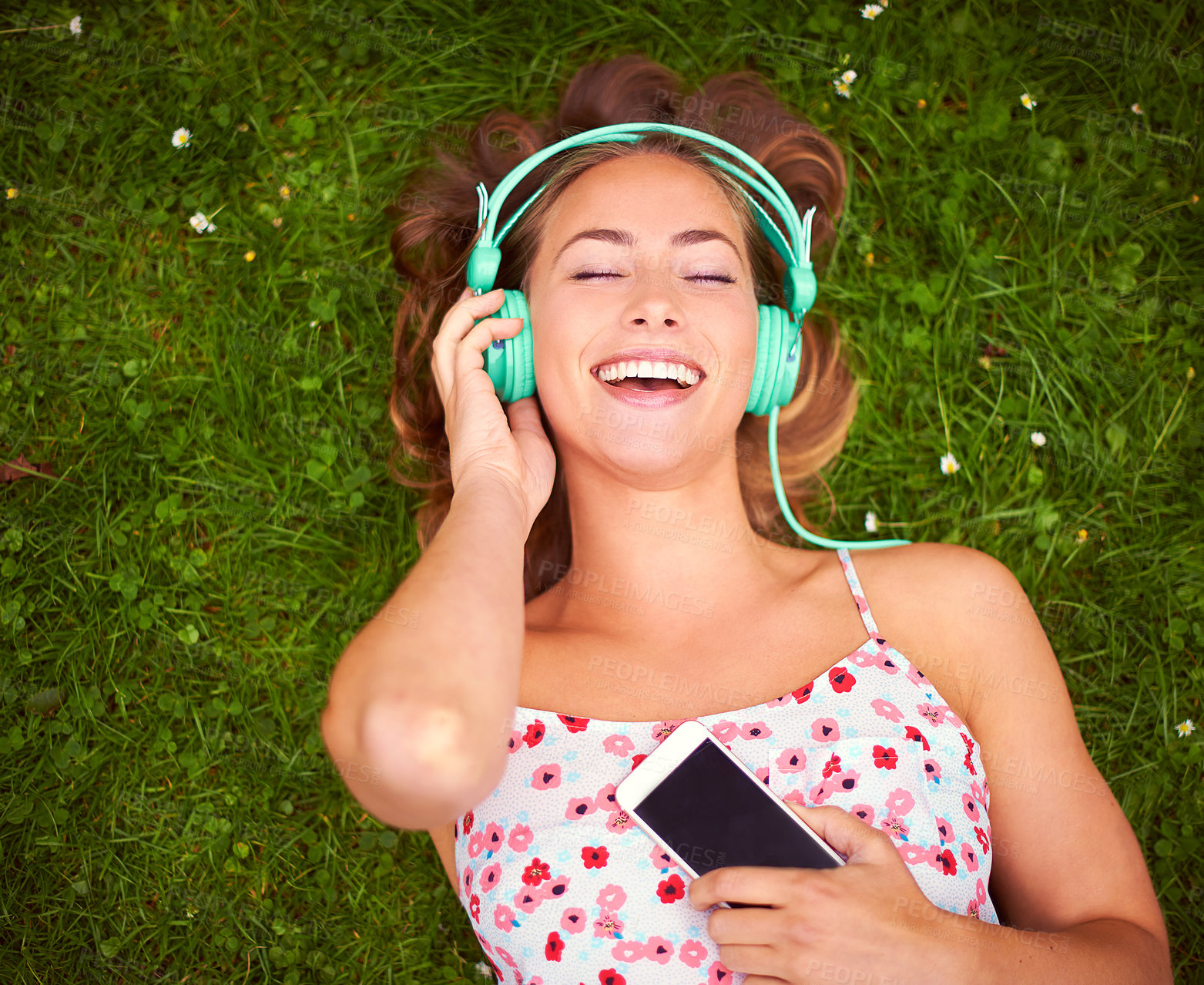 Buy stock photo Shot of a young woman listening to music while lying on the grass
