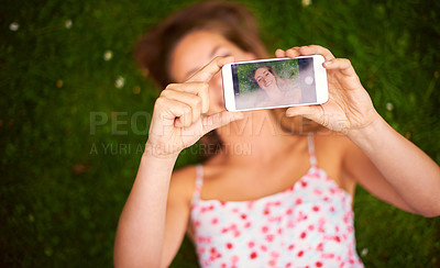 Buy stock photo Shot of a young woman taking a selfie while lying on the grass