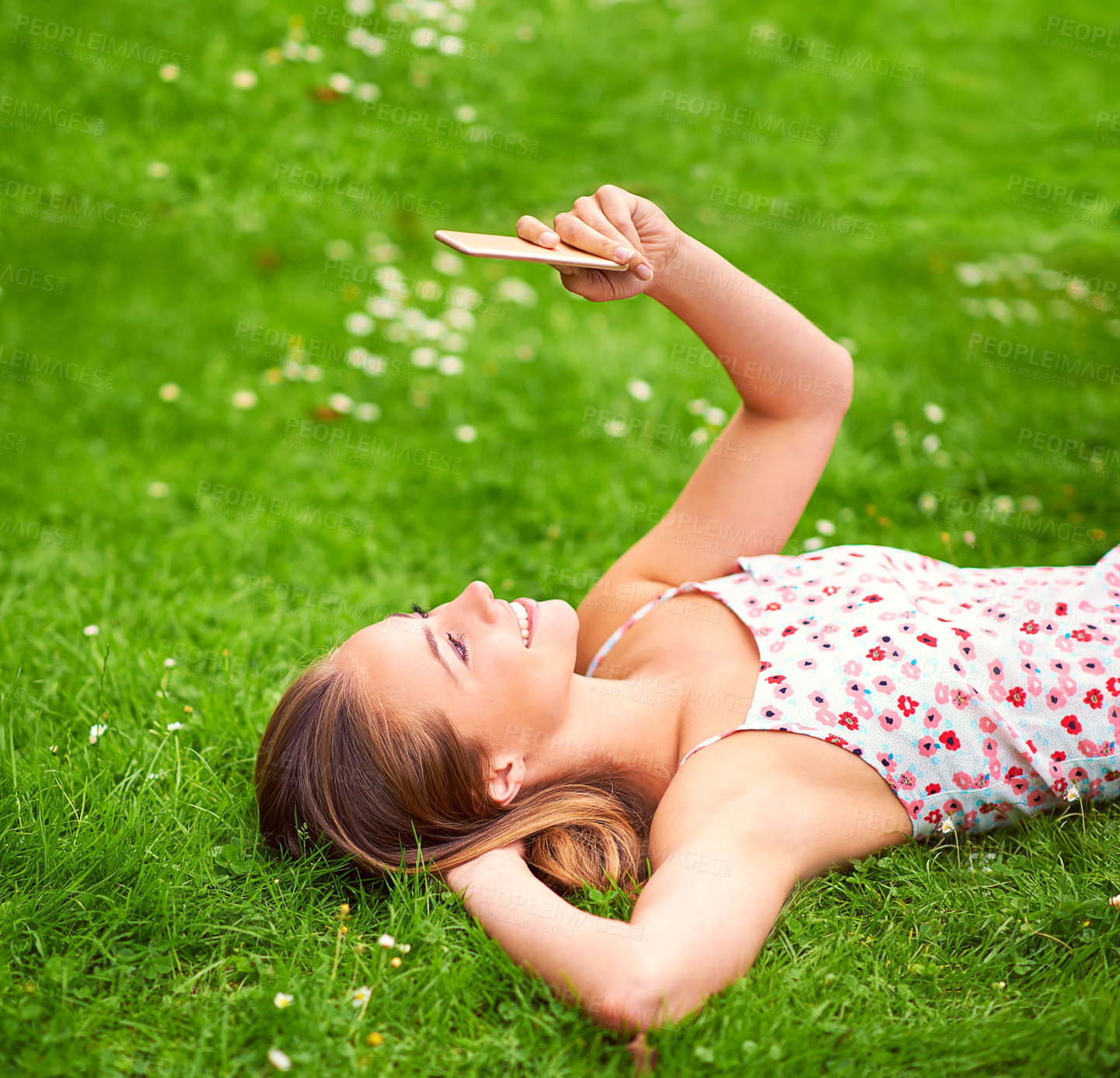 Buy stock photo Shot of a young woman using her cellphone while lying on the grass