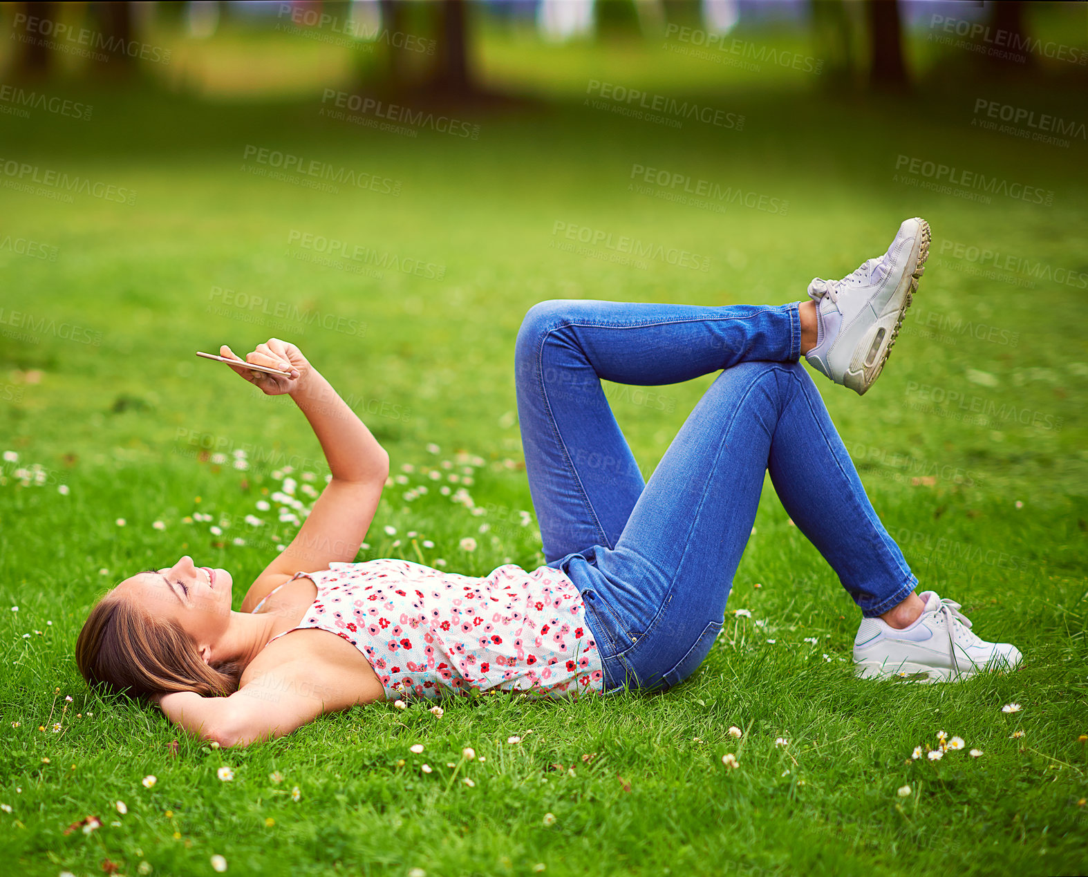 Buy stock photo Woman, phone and lying on lawn with reading, texting and smile for notification, chat and contact in spring. Girl, student and happy with smartphone on grass at campus to relax, click or social media