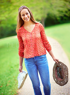 Buy stock photo Shot of a young woman walking in a park holding her shoes and a hat