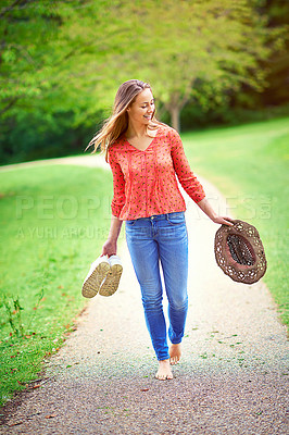 Buy stock photo Shot of a young woman walking in a park holding her shoes and a hat