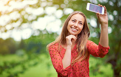 Buy stock photo Shot of a young woman taking a selfie outside