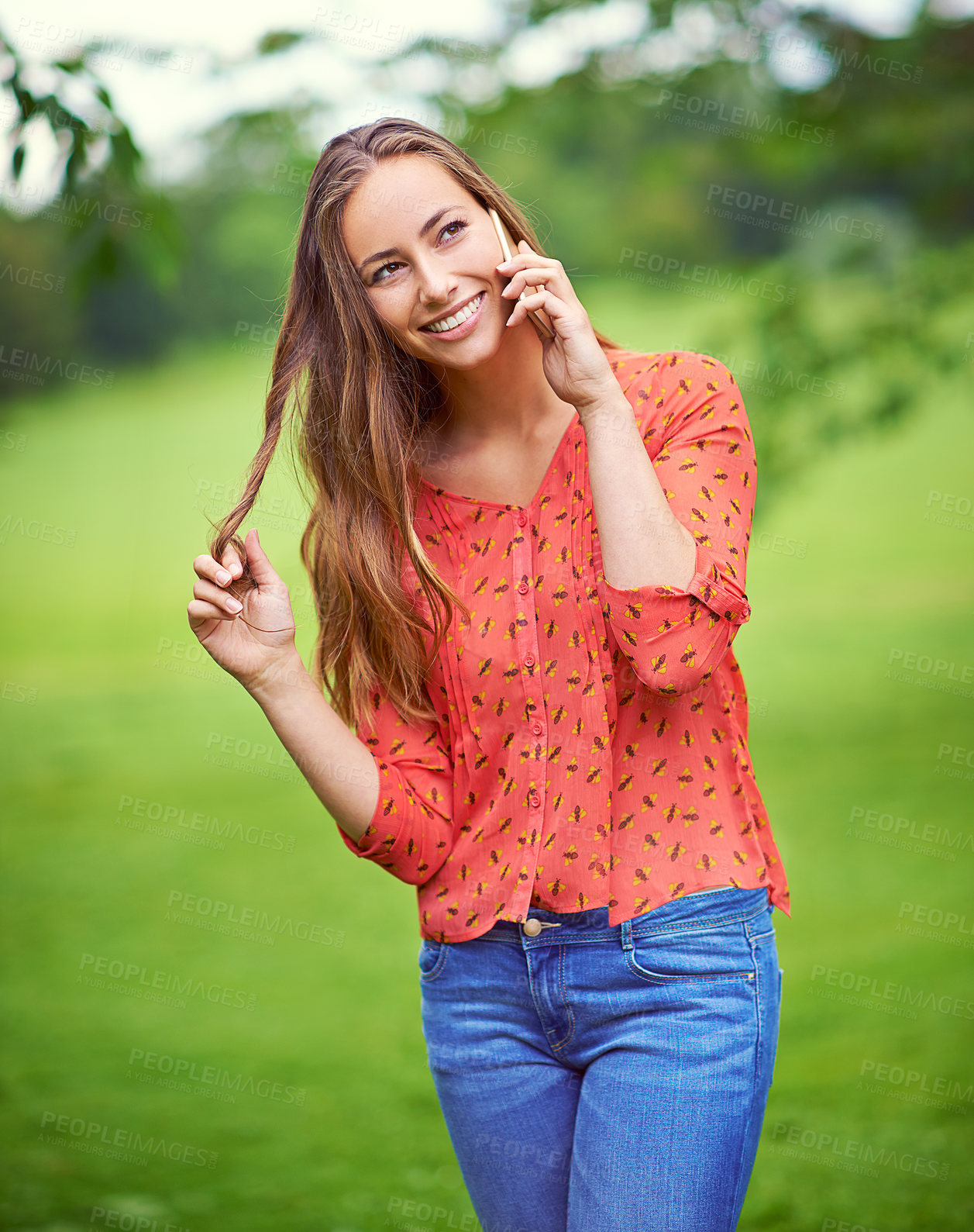 Buy stock photo Shot of a young woman twirling her hair while talking on her cellphone outside