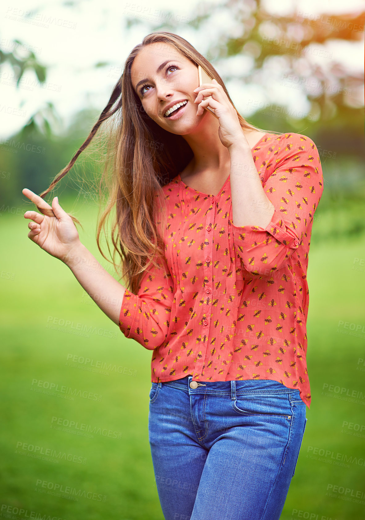 Buy stock photo Shot of a young woman twirling her hair while talking on her cellphone outside