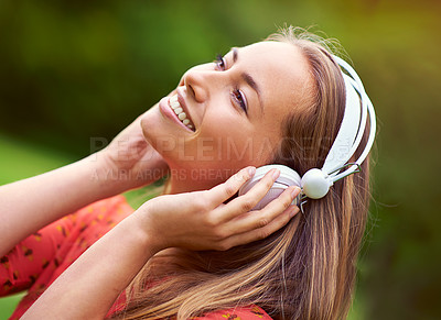 Buy stock photo Shot of a young woman listening to music through headphones in the outdoors
