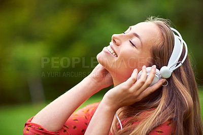 Buy stock photo Shot of a young woman listening to music through headphones in the outdoors