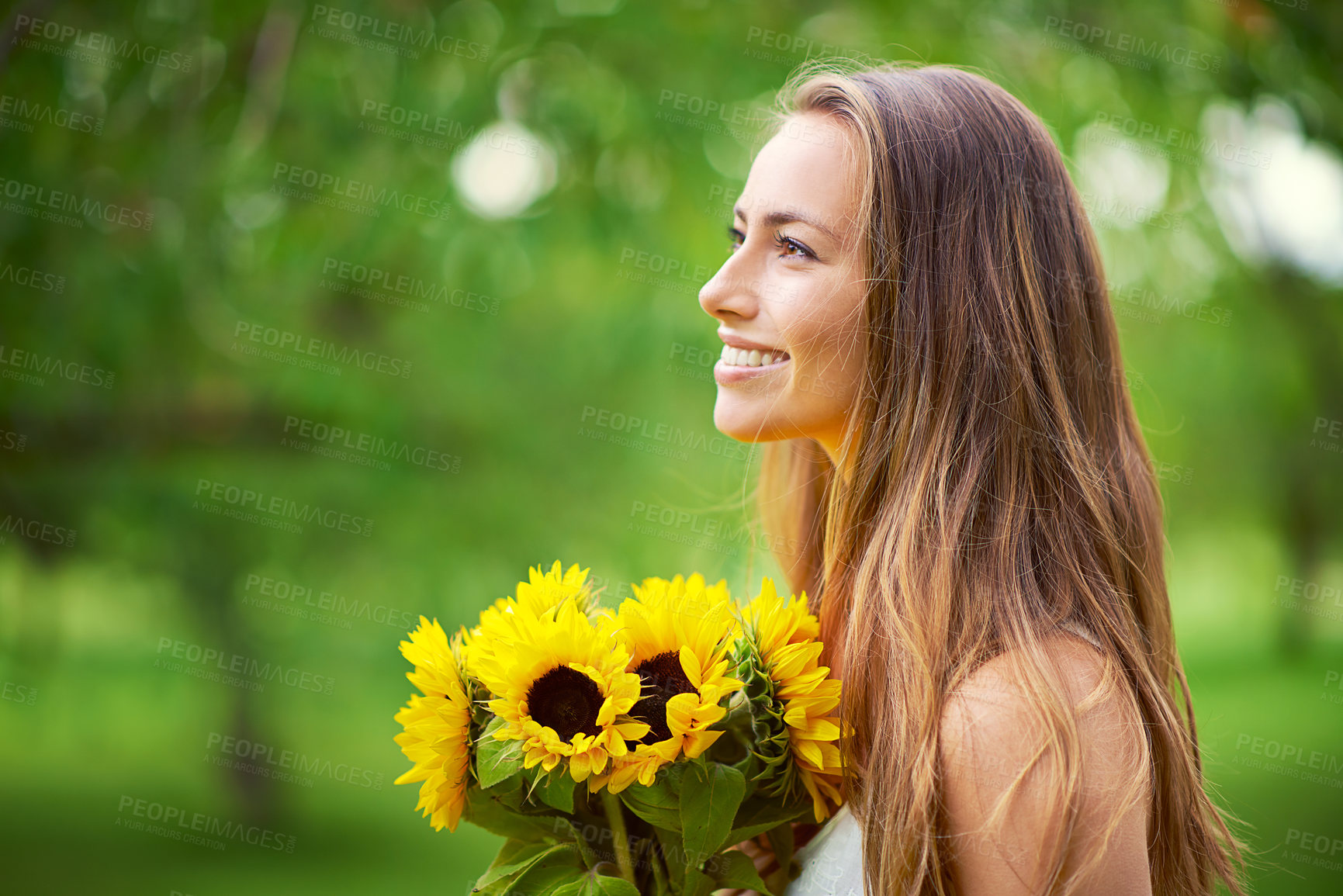 Buy stock photo Shot of a young woman holding a bunch of sunflowers outside