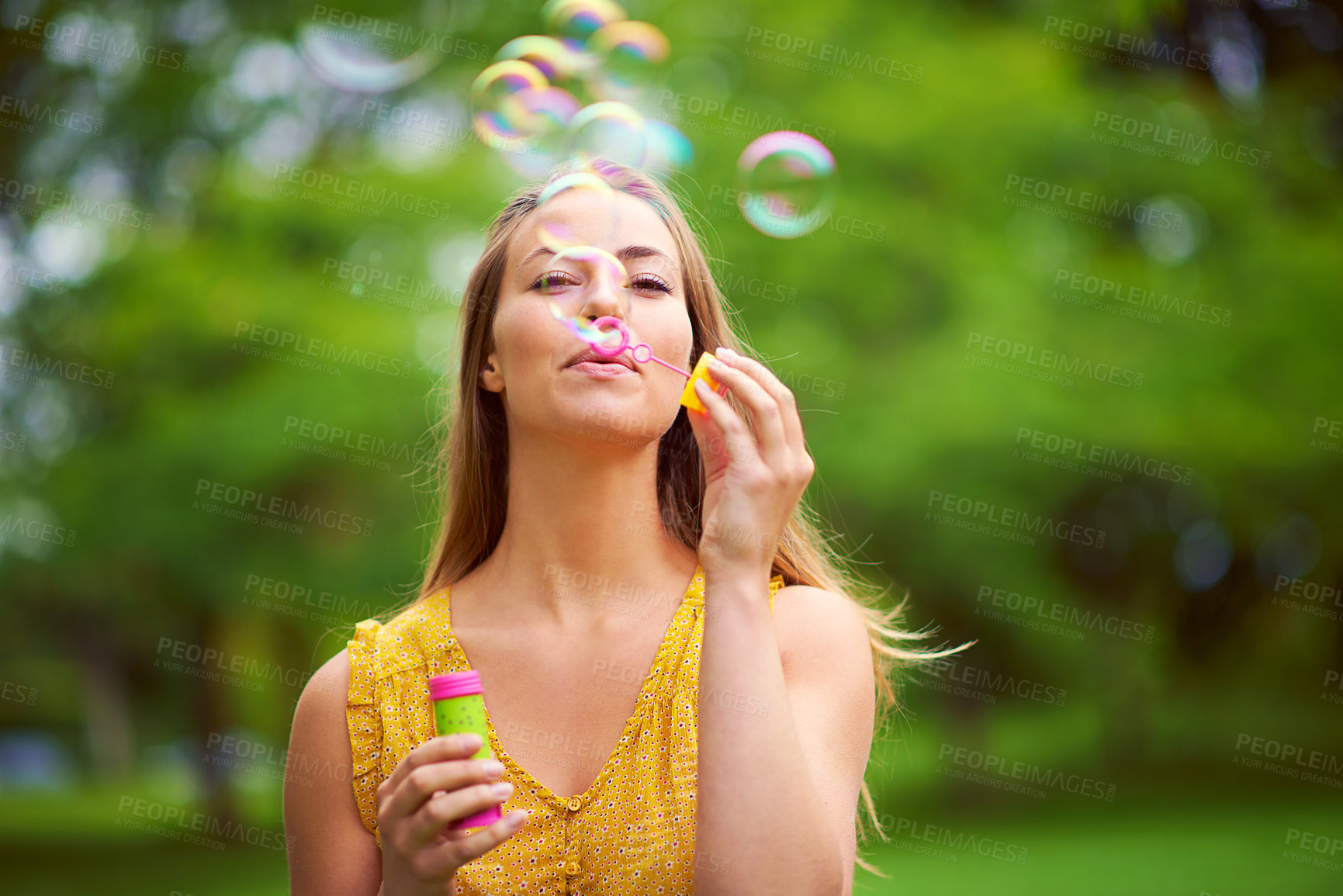 Buy stock photo Shot of a carefree young woman blowing bubbles in the park
