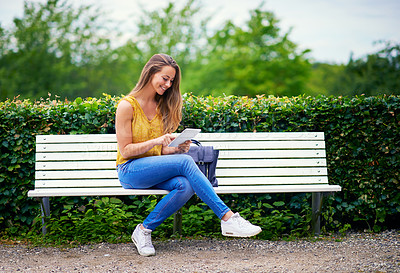Buy stock photo Shot of a young woman using a digital tablet on a park bench