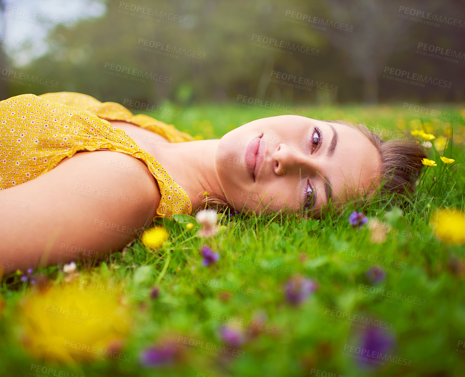 Buy stock photo Portrait of a young woman lying down in a field of grass and flowers