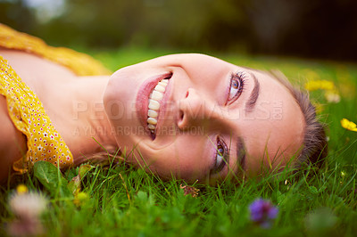 Buy stock photo Shot of a young woman lying down in a field of grass and flowers