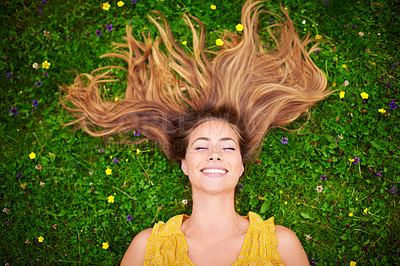 Buy stock photo High angle shot of a carefree young woman relaxing in a field of grass and flowers