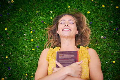 Buy stock photo High angle shot of a carefree young woman relaxing on the grass with a book