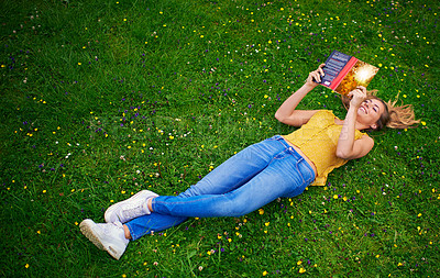 Buy stock photo Shot of a carefree young woman relaxing in a field of grass with a book