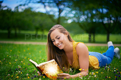 Buy stock photo Shot of a carefree young woman relaxing at the park with a book