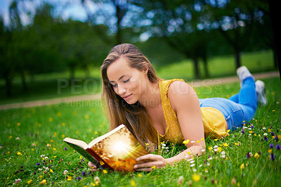Buy stock photo Shot of a carefree young woman relaxing in a field of grass with a book