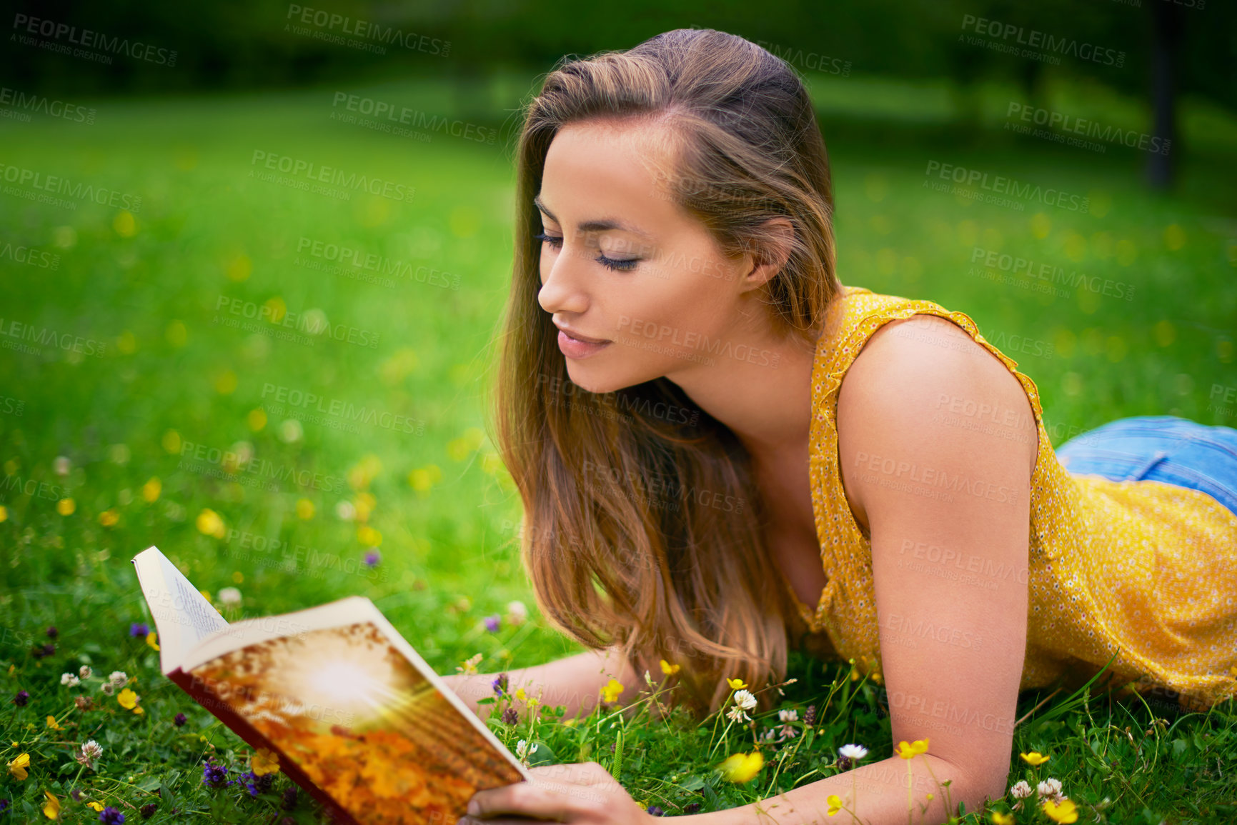 Buy stock photo Shot of a carefree young woman relaxing in a field of grass with a book