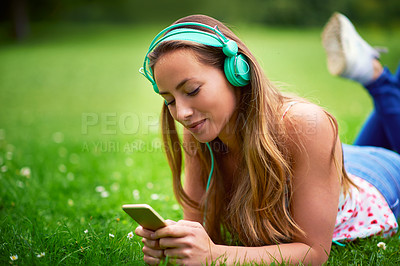 Buy stock photo Shot of a young woman listening to music while lying on the grass at the park