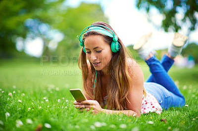 Buy stock photo Smartphone, woman and headphones on grass for music, streaming and audio book or podcast. College student, technology and happy on campus or garden for network, online and media for education in park