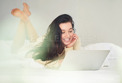 Buy stock photo Cropped shot of a young woman using her laptop while lying on her bed
