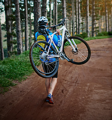 Buy stock photo Shot of a male cyclist walking along a trail carrying his mountain bike