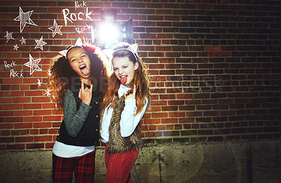 Buy stock photo Shot of two girls pulling faces and making a rock gesture