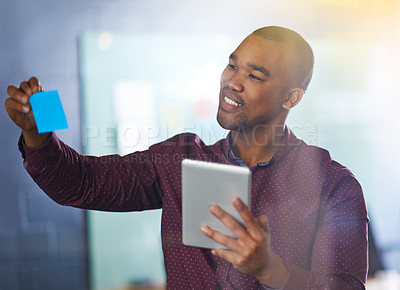 Buy stock photo Shot of a male designer holding a tablet looking at sticky notes on a glass wall