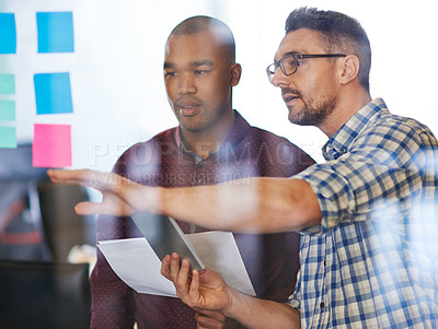 Buy stock photo Shot of two designers brainstorming at a glass wall filled with sticky notes