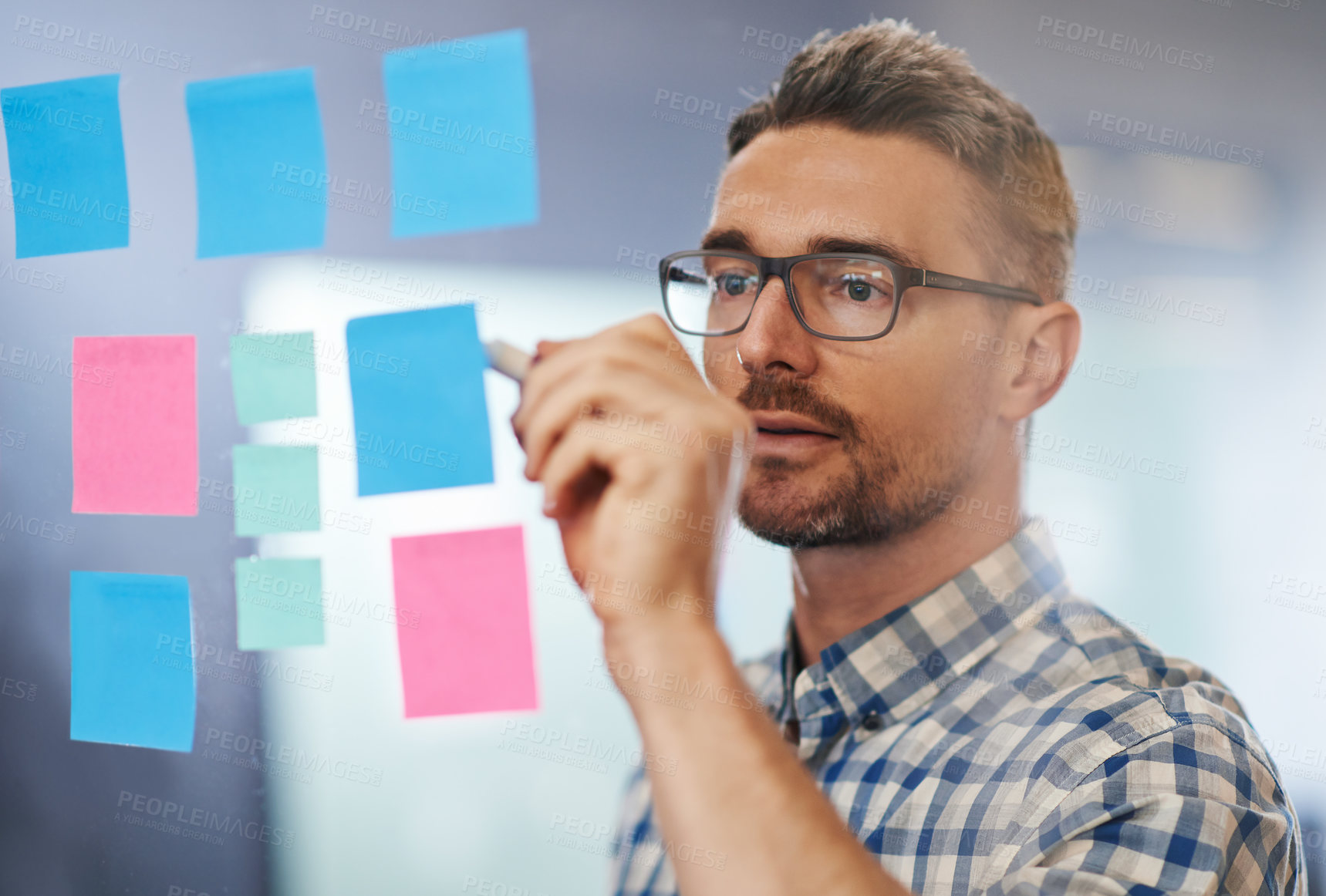 Buy stock photo Shot of a male designer writing on sticky notes stuck a glass wall