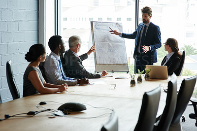 Buy stock photo Confident businessman leading a presentation on a whiteboard with diverse colleagues in an office boardroom meeting. Manager pointing to research and marketing data, planning a strategy with his team