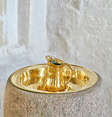 Buy stock photo Closeup of one gold and brass baptism jug on a tray in a church. A sacred pitcher used for pouring water at christening ceremonies. An antique baptismal font in the Danish National Church in Denmark