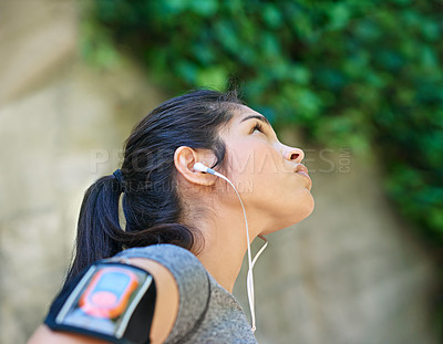 Buy stock photo Shot of a sporty young woman listening to music while exercising outside