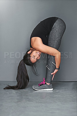 Buy stock photo Shot of a fit young woman stretching against a gray background