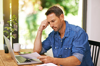 Buy stock photo Shot of a man looking over some paperwork while working from home