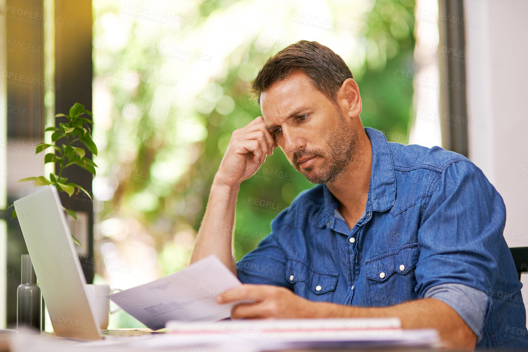 Buy stock photo Shot of a man looking over some paperwork while working from home