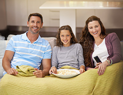 Buy stock photo Shot of a family sitting on their living room sofa watching a movie and eating popcorn