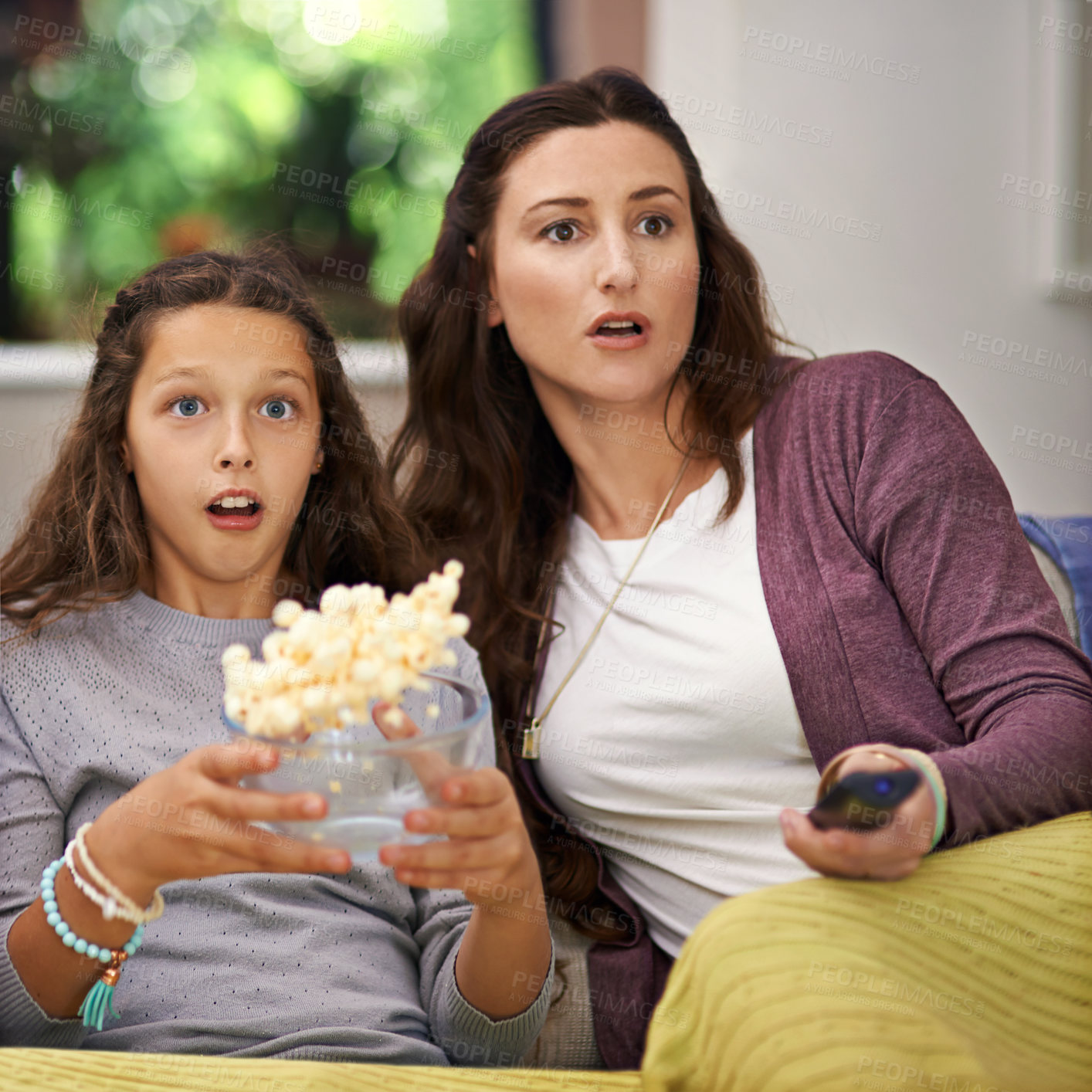 Buy stock photo Shot of a mother and daughter sitting on their living room sofa watching a movie and eating popcorn