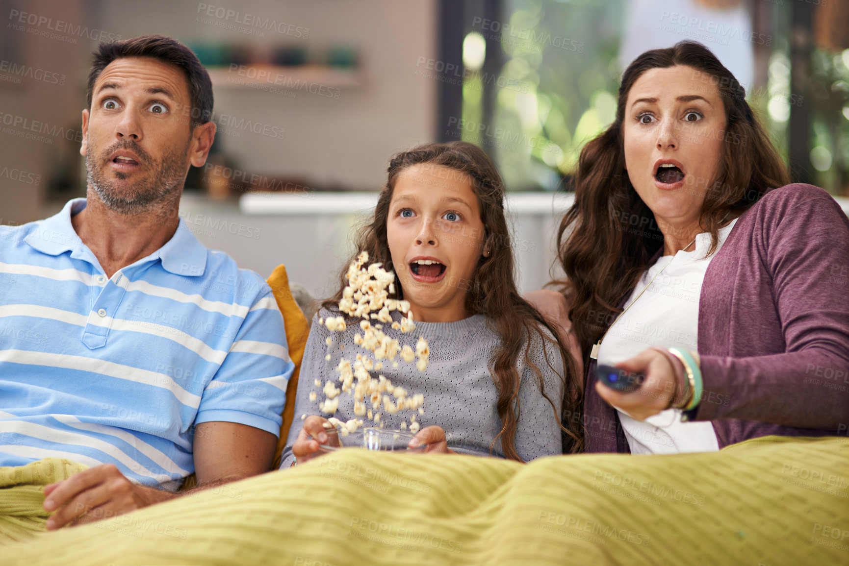 Buy stock photo Shot of a family sitting on their living room sofa watching a movie and eating popcorn