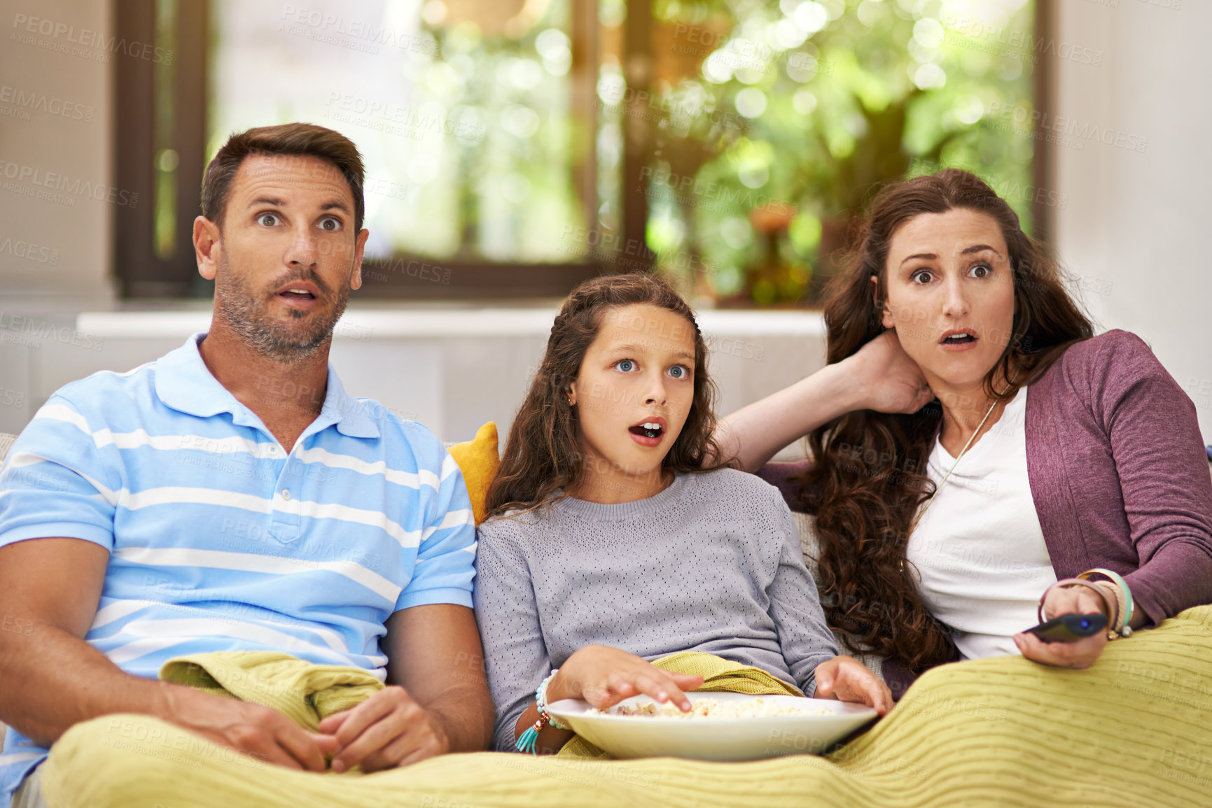 Buy stock photo Shot of a family sitting on their living room sofa watching a movie and eating popcorn