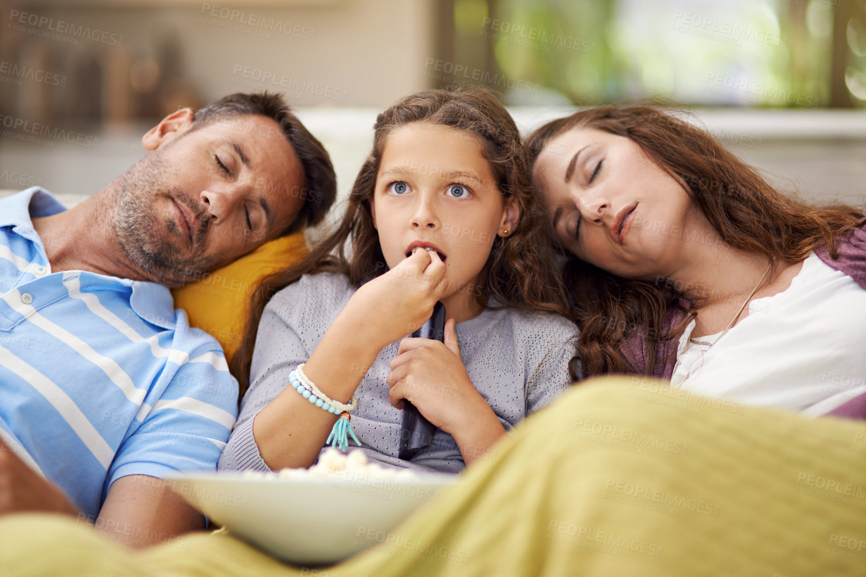 Buy stock photo Shot of a girl sitting on the living room watching a movie with her parents asleep beside her