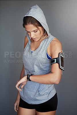 Buy stock photo Shot of a sporty young woman checking the time on her sports watch against a gray background