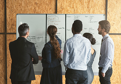 Buy stock photo Rearview shot of a group of businesspeople looking over plans on a whiteboard