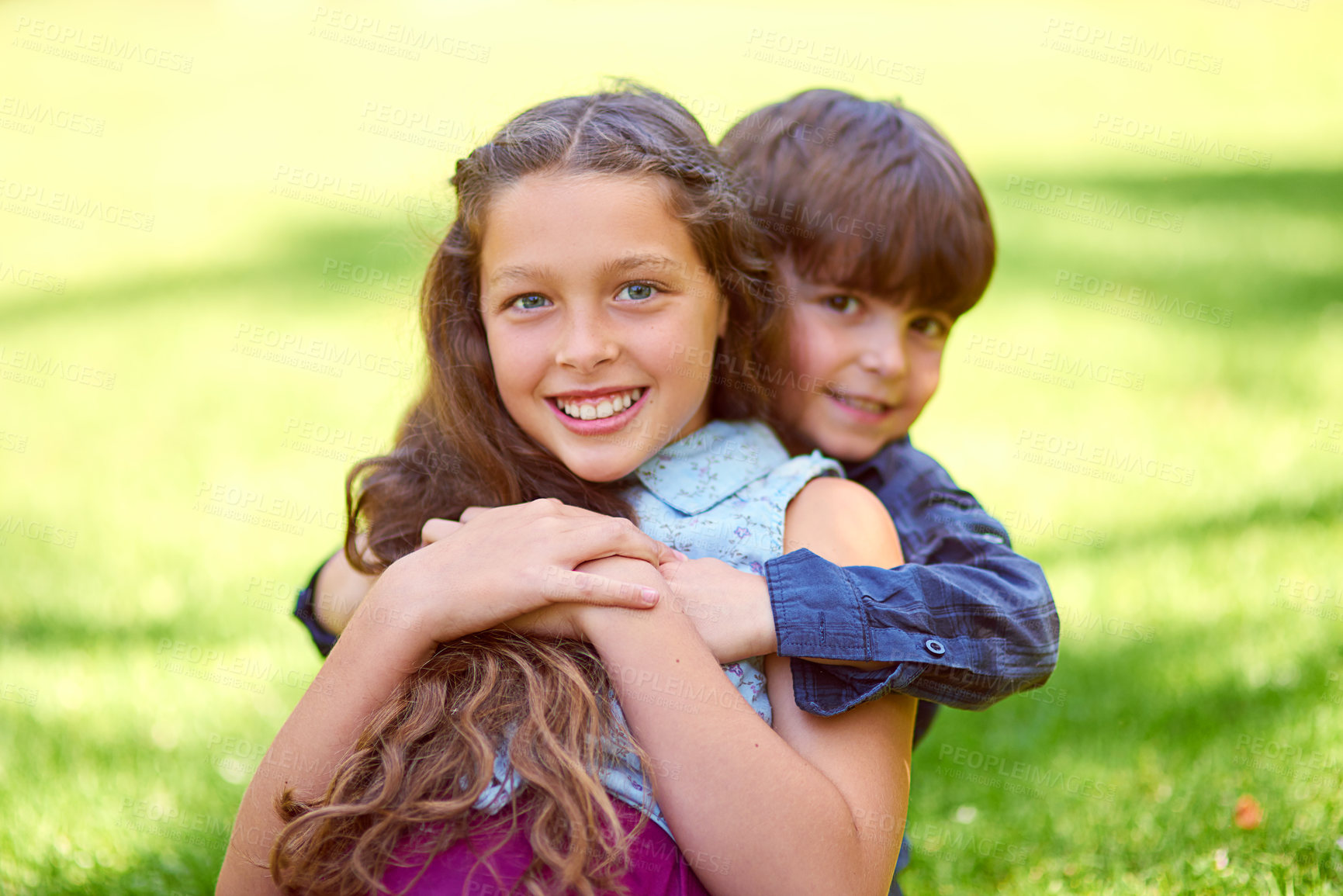 Buy stock photo Cropped shot of a young boy embracing his sister while sitting on the grass outside